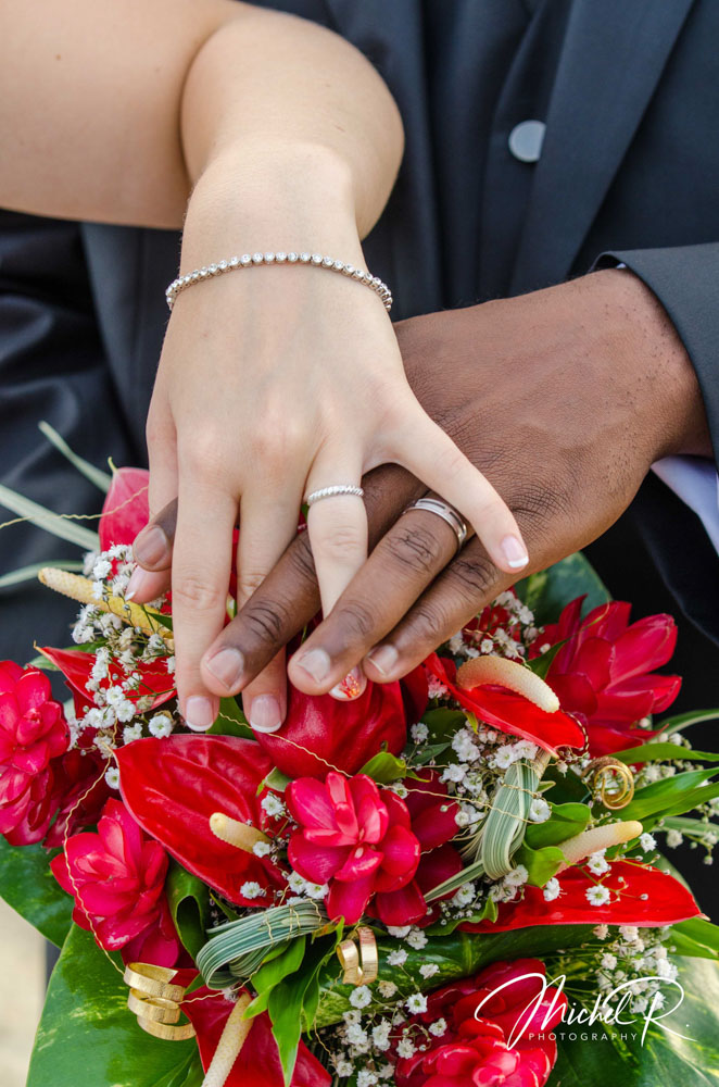 Mains de jeunes mariés posées sur un bouquet rouge