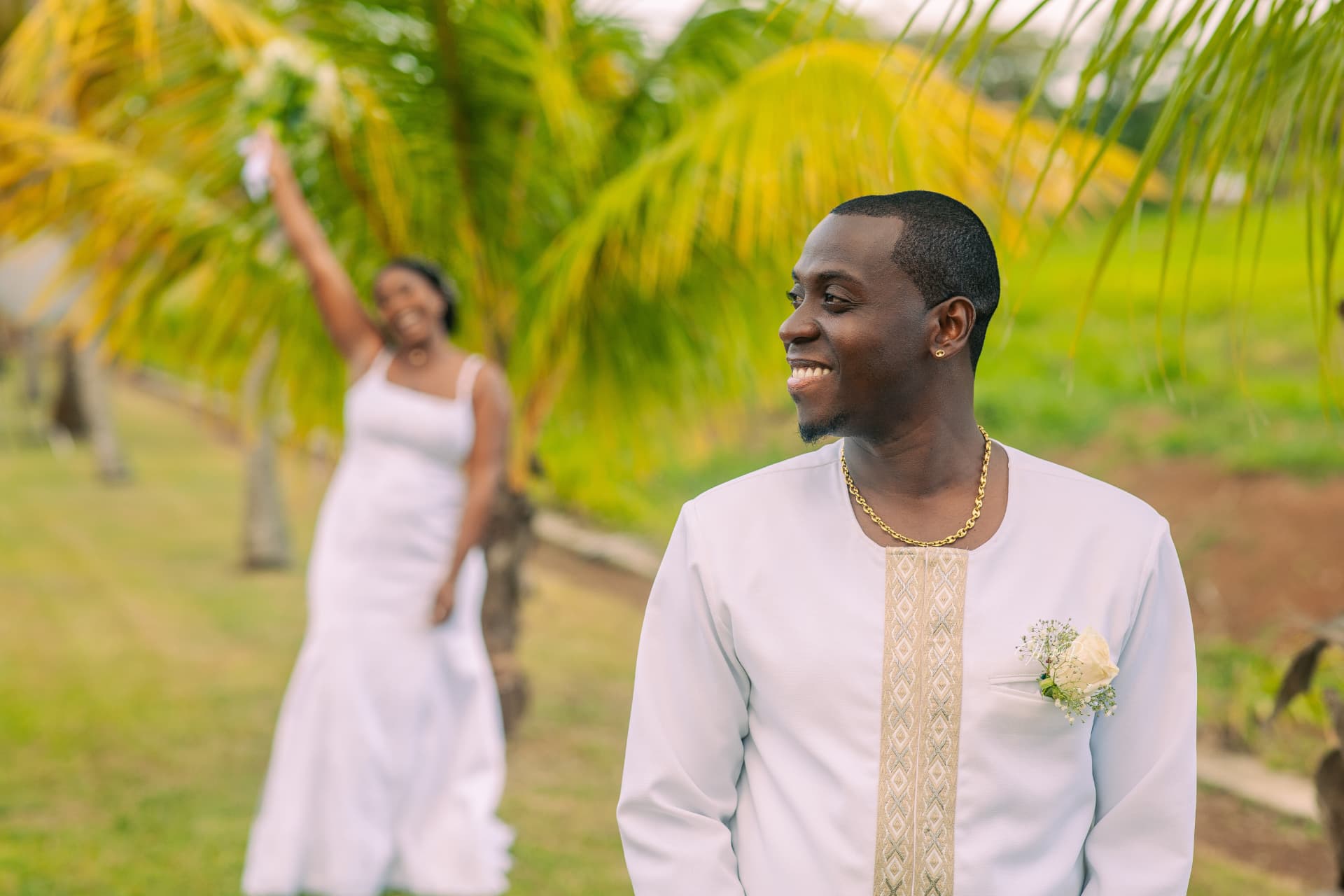 Marié souriant avec la mariée au second plan sous les palmiers